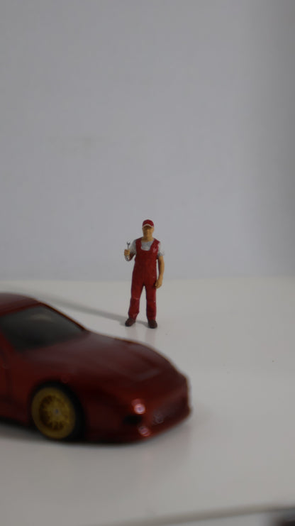Figura mecánico miniatura 1:64 junto a auto die-cast para escala de referencia
