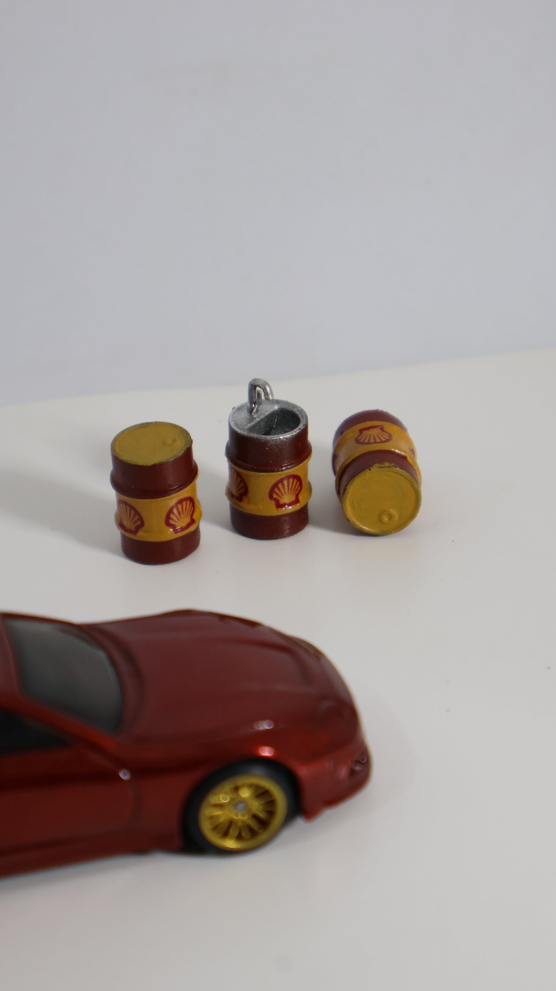 Barriles Shell miniatura 1:64 junto a auto die-cast para escala de referencia